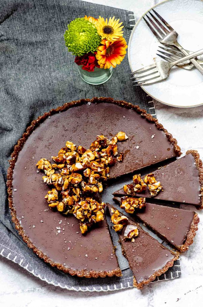 Overhead view of a chocolate tart topped with caramelized hazelnuts and with 3 cut slices