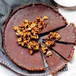 Overhead view of a chocolate tart topped with caramelized hazelnuts and with 3 cut slices