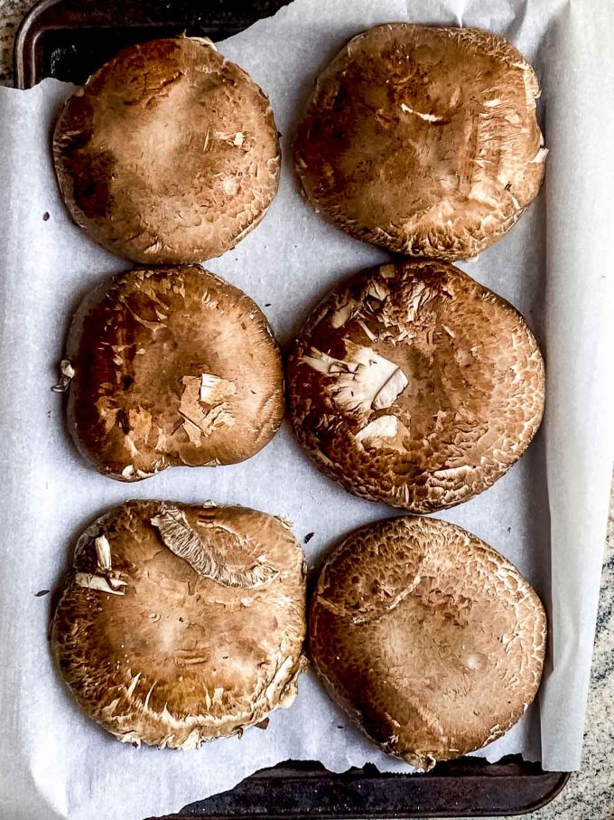6 portobello mushrooms on a baking sheet that is lined with parchment paper 