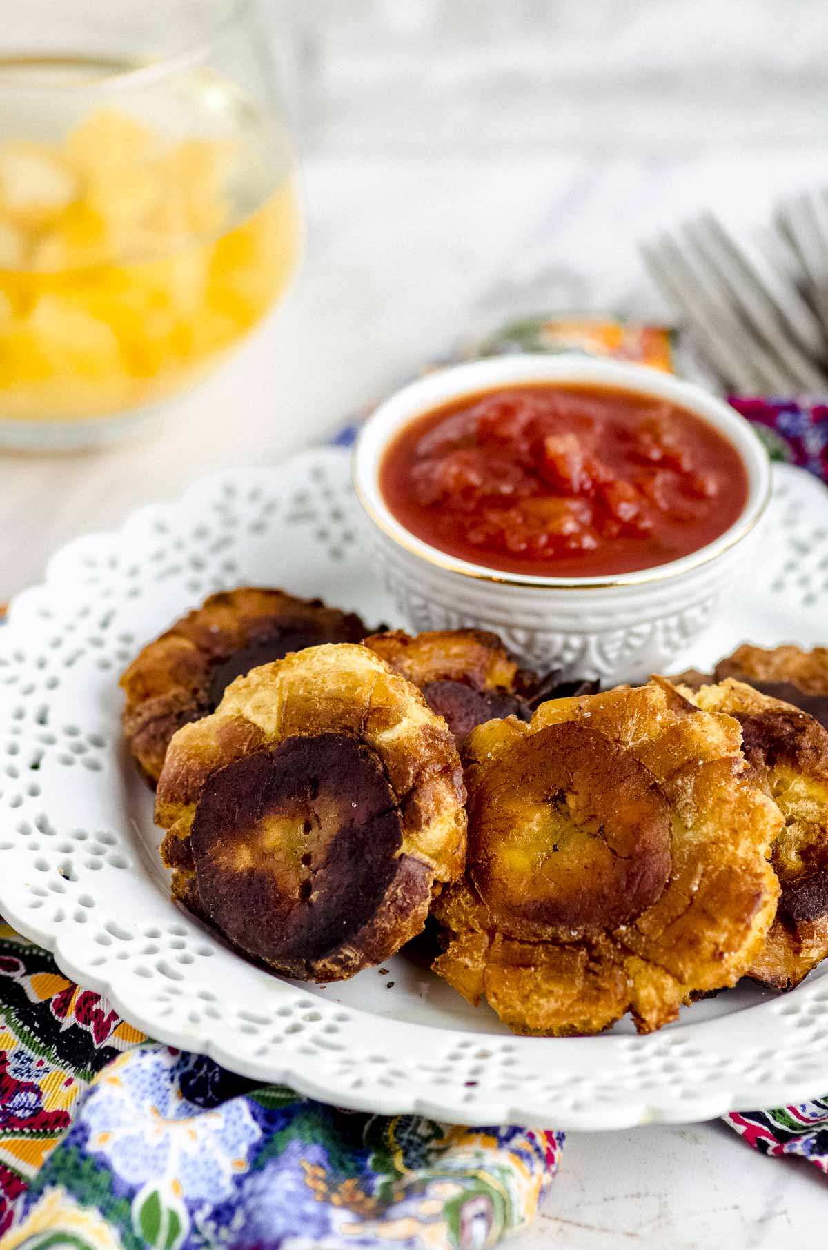 Close-up side view of a white plate with tostones and a small bowl with red salsa