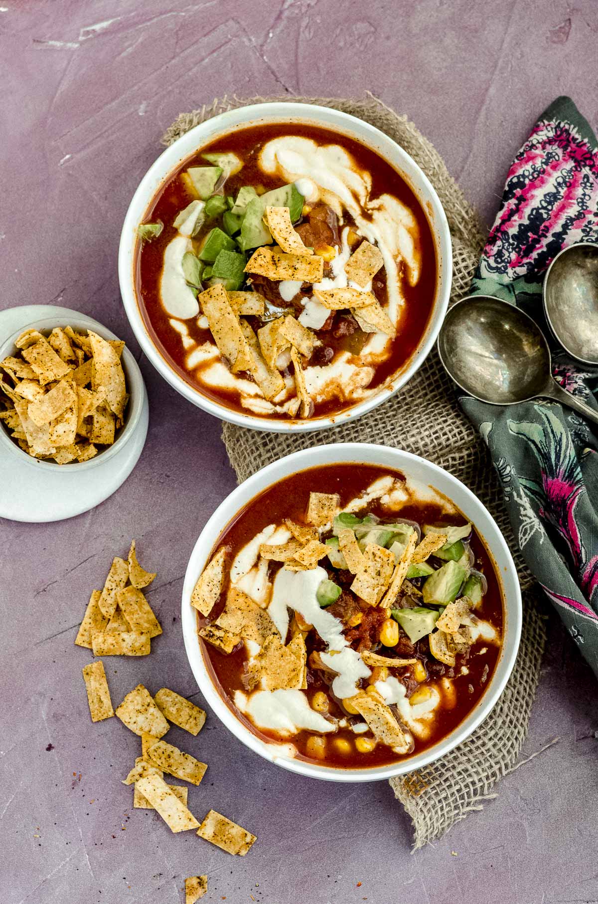 Overhead view of two tortilla soup bowls topped with avocado, tortilla chips and vegan sour cream