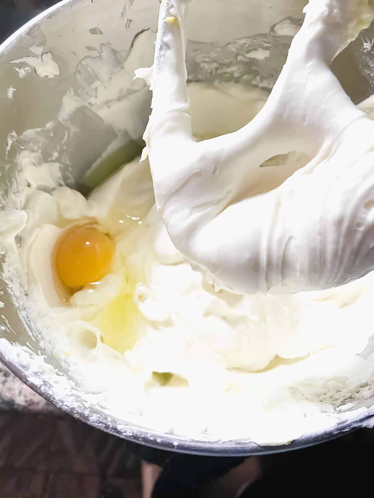 Adding egg one at a time to a cream cheese mixture