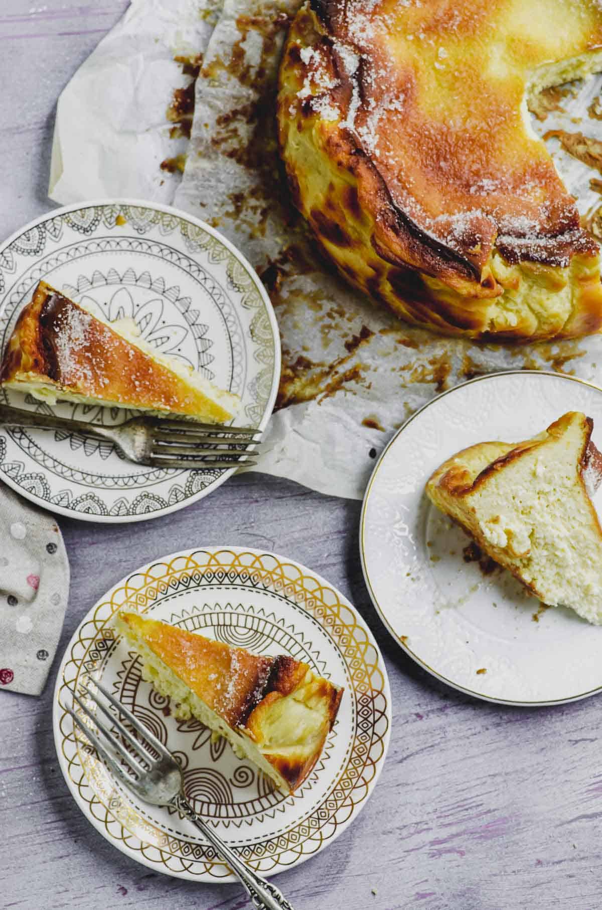 Overhead partial view of a burnt Basque cheesecake next to 3 plates with slices of the cheesecake