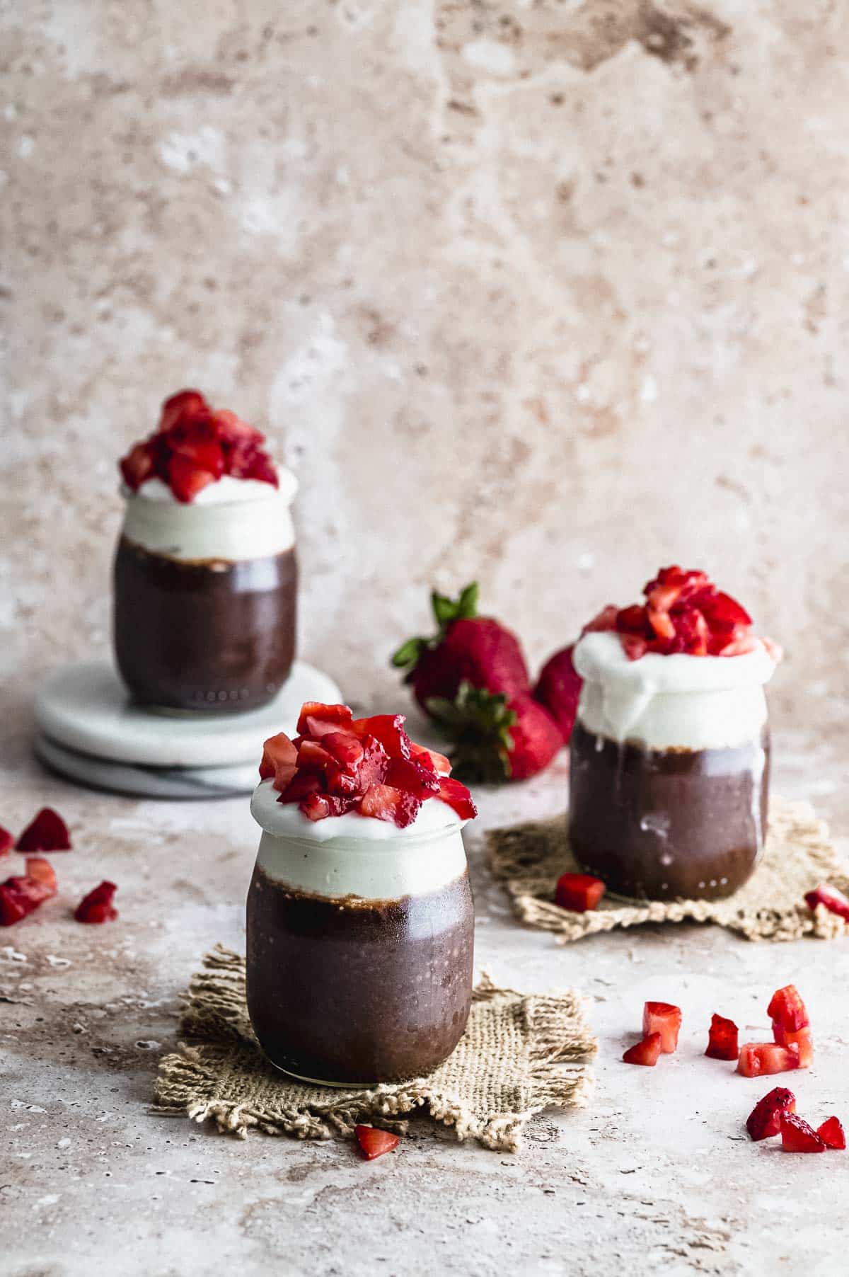 three jars with chocolate chia seed pudding topped with yogurt and strawberries

