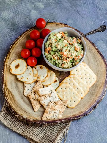 Birdseye view of a bowl with chickpea salad on a wood board with assorted crackers and fresh cherry tomatoes