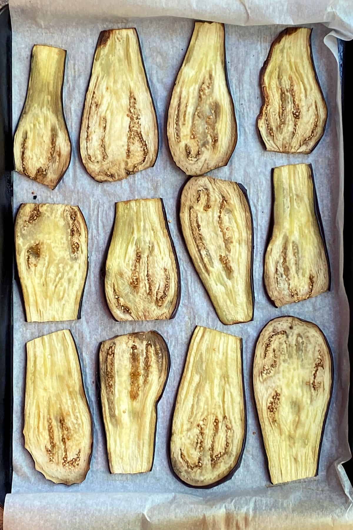 An overhead view of a parchment paper lined cookie sheet with baked slices of eggplant