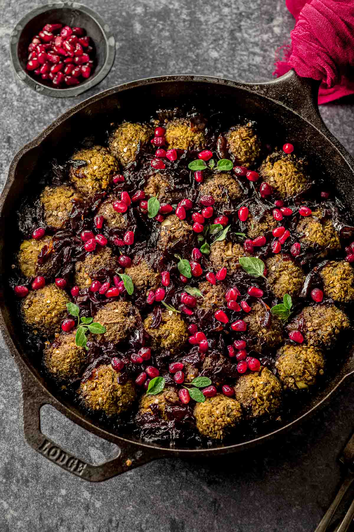 Overhead view of a cast iron pan with eggplant meatballs topped with pomegranate seeds