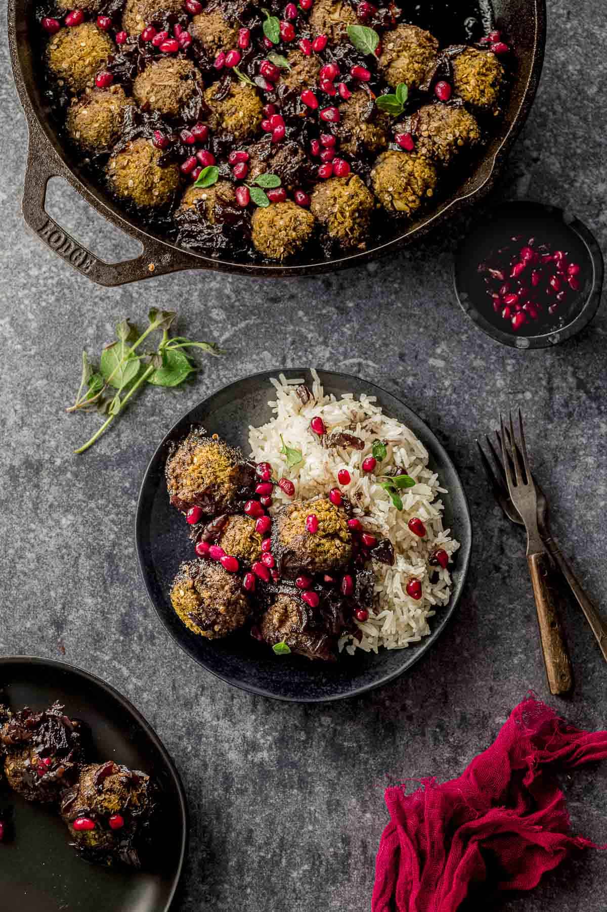 A pan and two plates with eggplant meatballs with pomegranate sauce