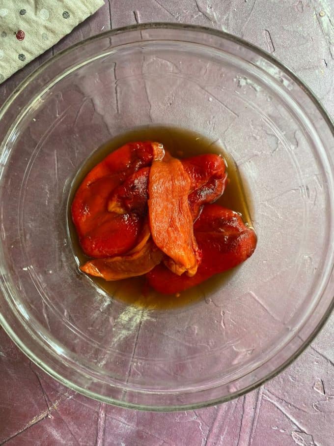 A view of sliced roasted red pepper placed in olive oil in a glass bowl