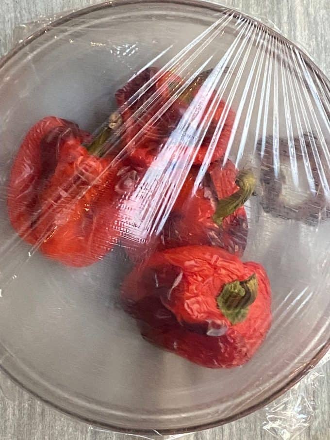 An overhead view of a bowl with roasted red peppers with plastic wrap over it