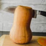 A standing butternut squash with a knife going through it