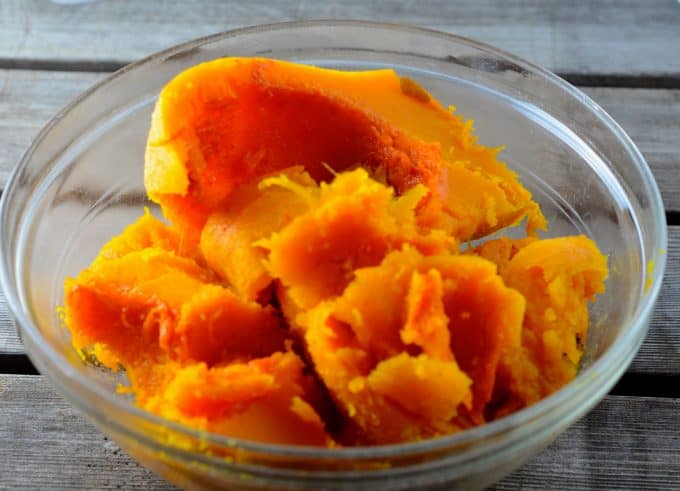 Roasted butternut flesh in a clear glass bowl on a wooden surface