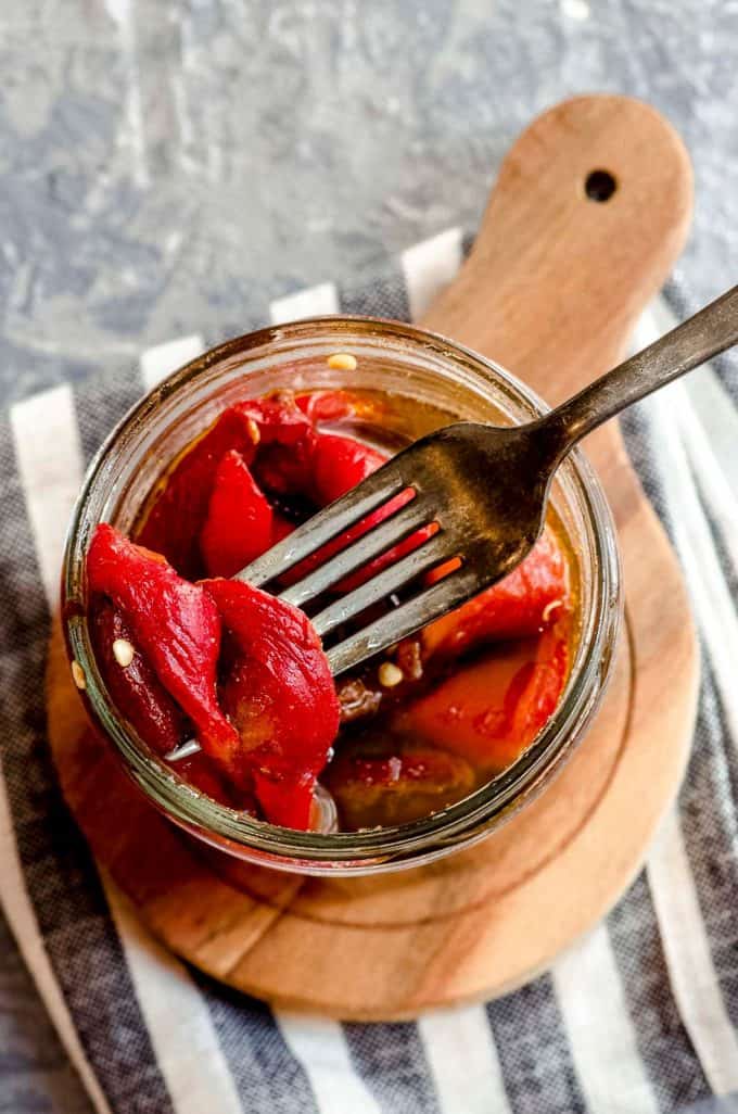 An overhead view of a jar of roasted red peppers with a fork with a pepper on it