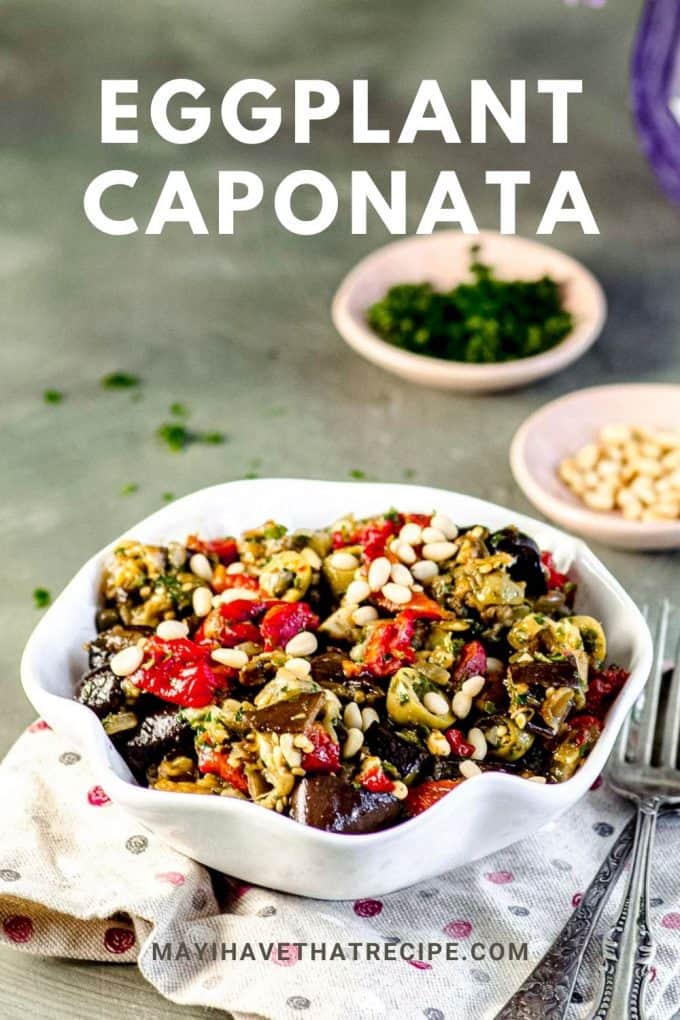An tilted view of a white bowl with eggplant caponata with chopped parsley and pine nuts in separate bowls