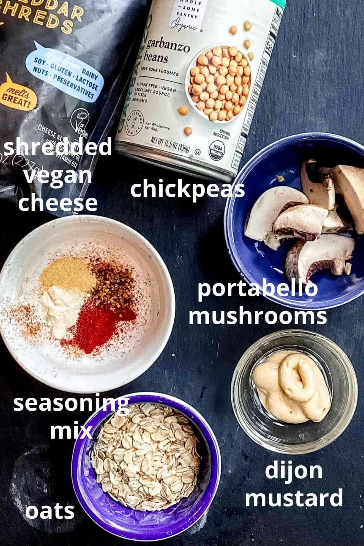 An overhead view of ingredients to make veggie meatballs; shredded vegan cheese, a can of chickpeas, portabello mushrooms, seasoning mix, dijon mustard and oats