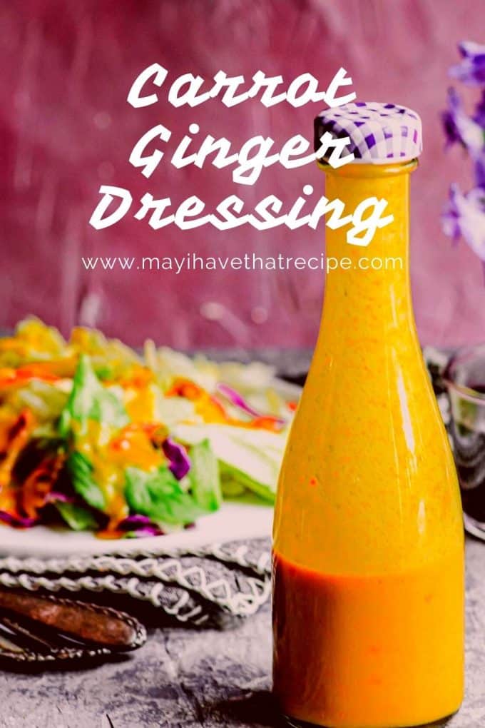 A glass carafe with carrot ginger dressing in it with a salad in the background