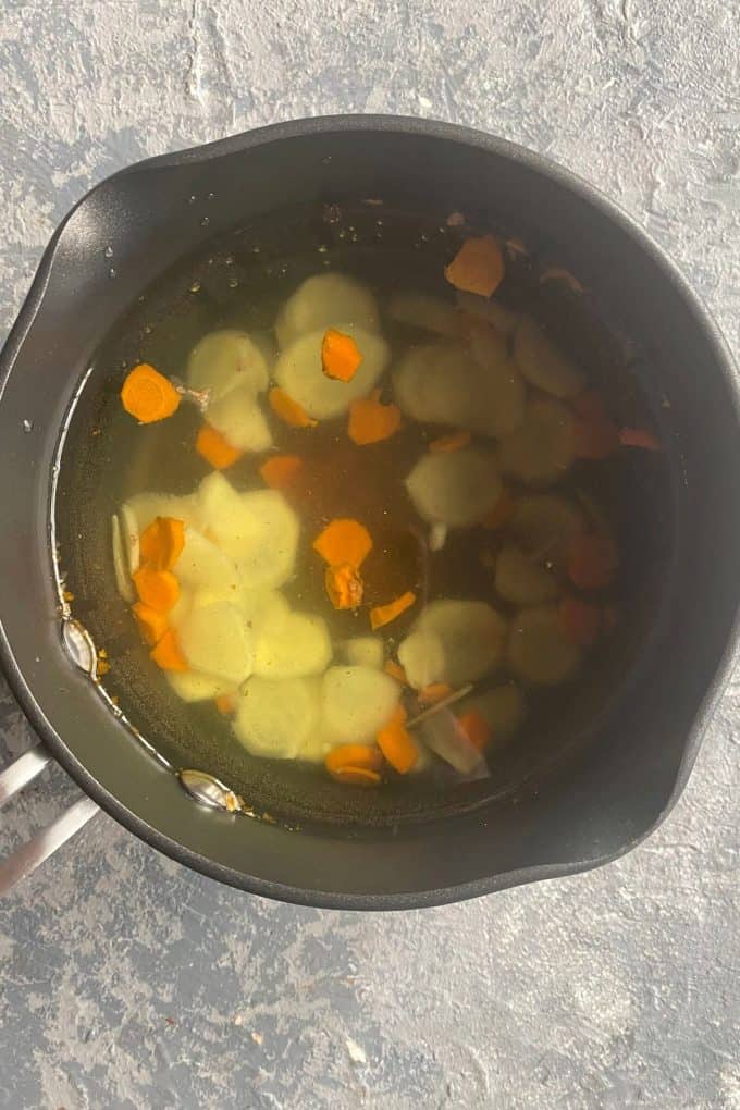 A pot with water and ginger and turmeric root pieces floating to the top