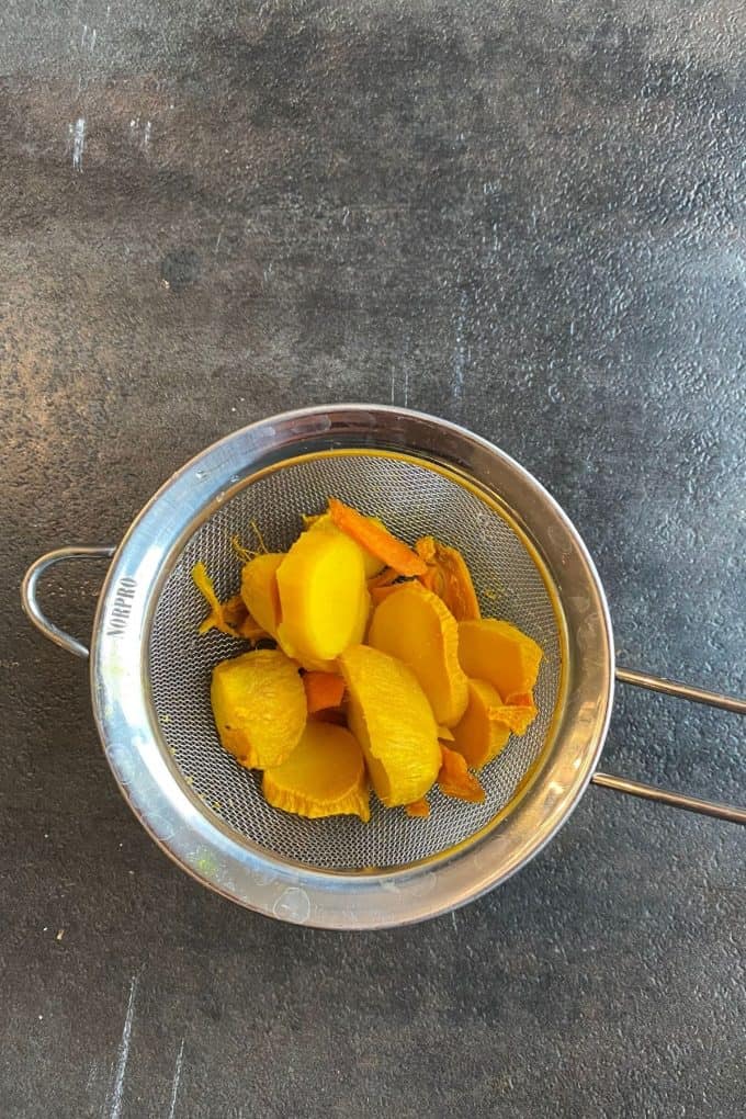 A metal mesh strainer with pieces of turmeric root and ginger