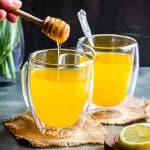 Ginger Turmeric Tea in two clear glass mugs with honey being drizzle above one of the mugs