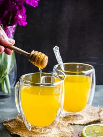 Ginger Turmeric Tea in two clear glass mugs with honey being drizzle above one of the mugs
