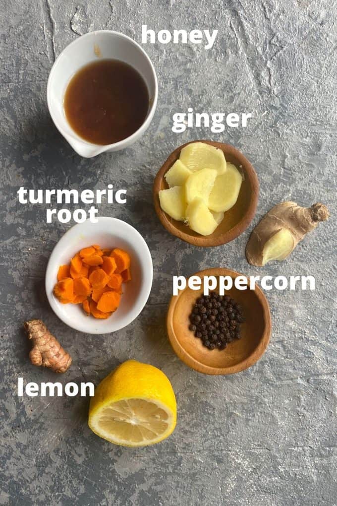 The ingredients to make ginger turmeric tea; honey, ginger, turmeric root, peppercorn, and lemon