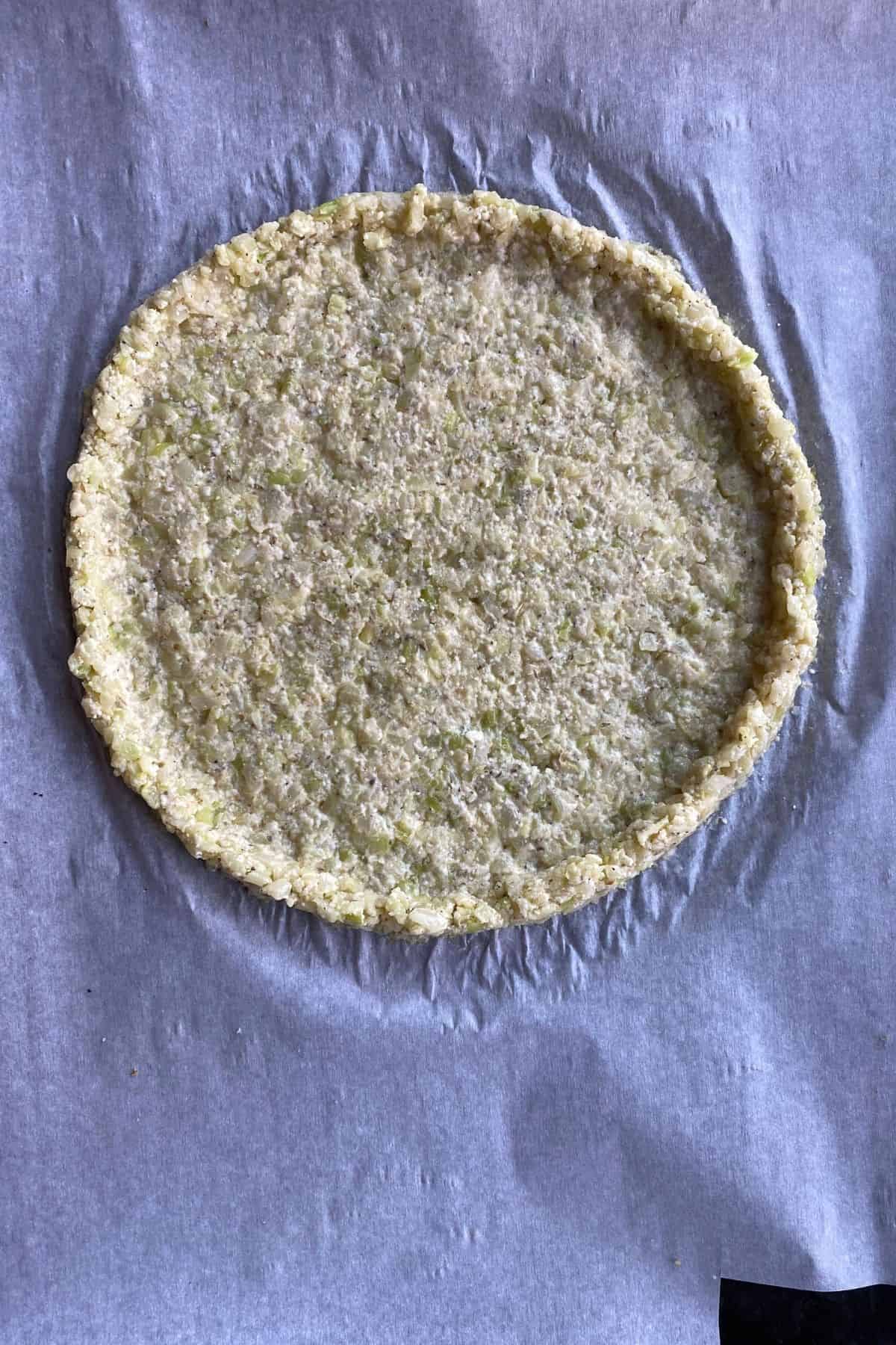 Cauliflower crust before baked pressed into a circle on parchment paper
