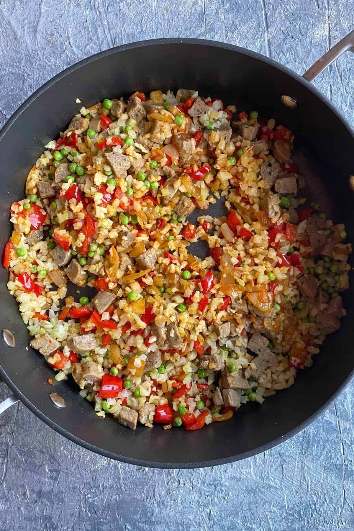A pan of pans with sauteed cauliflower rice, red peppers, scallions, and onions