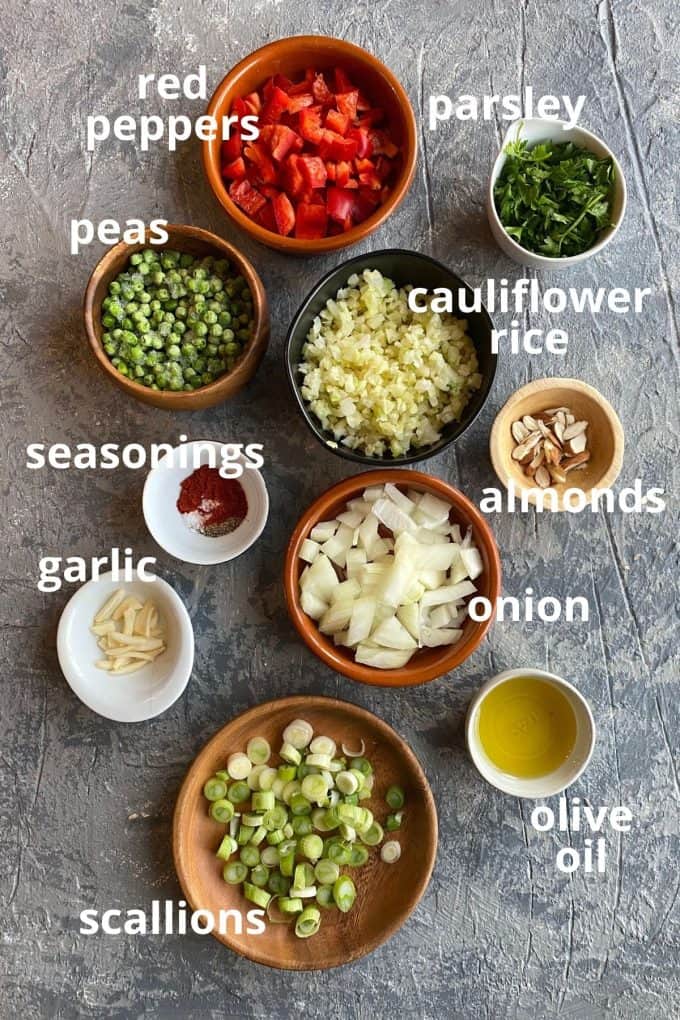 The ingredients to make cauliflower rice; red peppers, parsley, peas, cauliflower rice, seasonings, almonds, onions, garlic, olive oil, and scallions