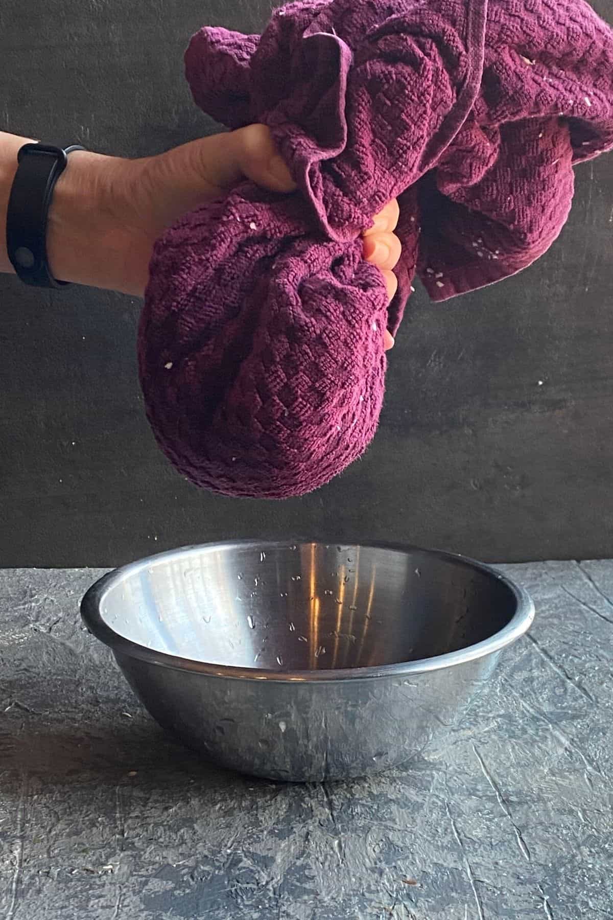 A purple cheesecloth of cauliflower being hand squeezed over a bowl
