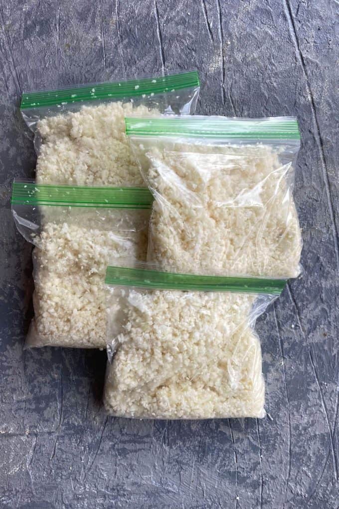 four resealable plastic sandwich storage bags filled with cauliflower rice
