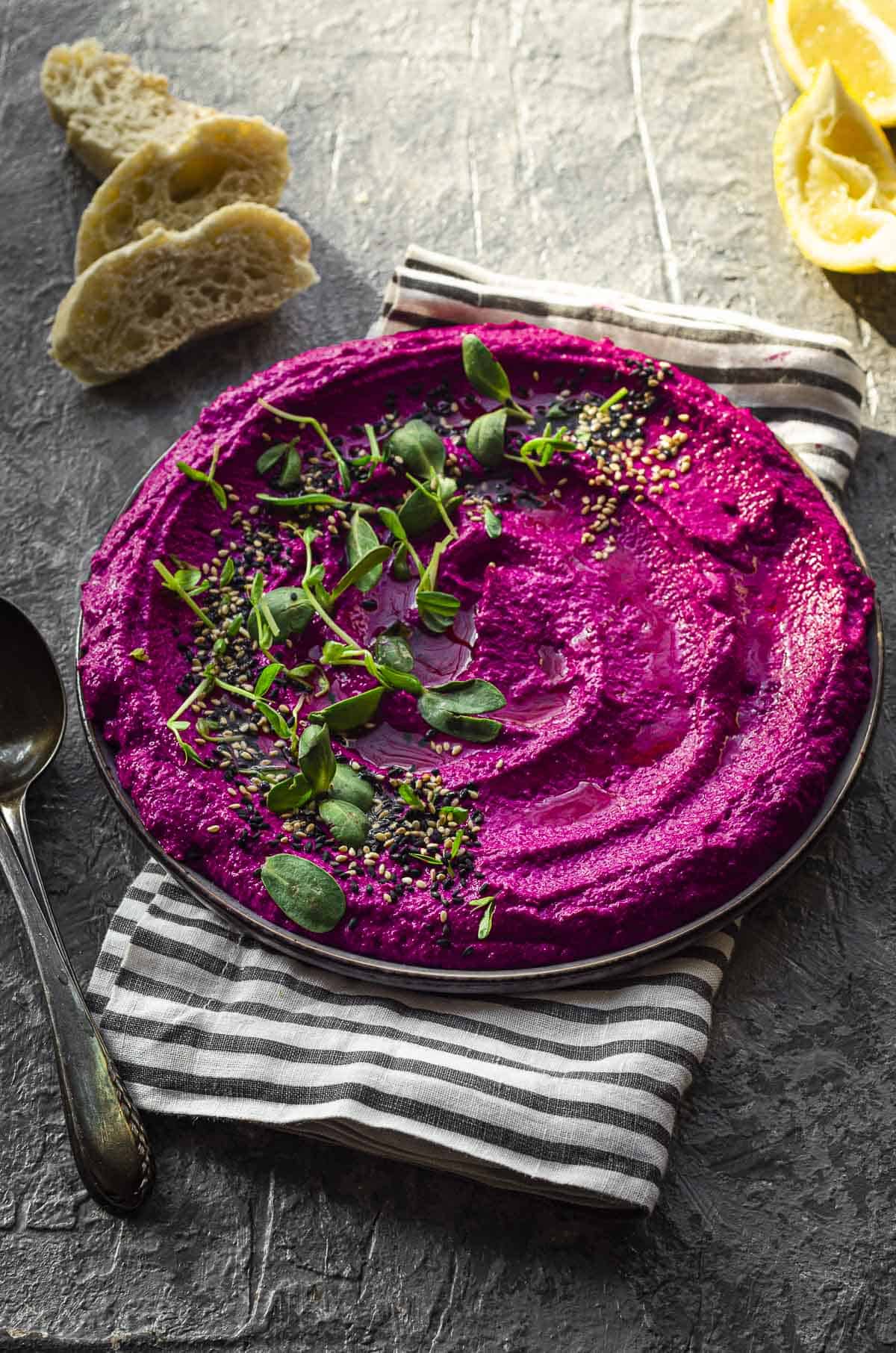 Side view  a plate with beet hummus topped with sesame seeds and sprouts
