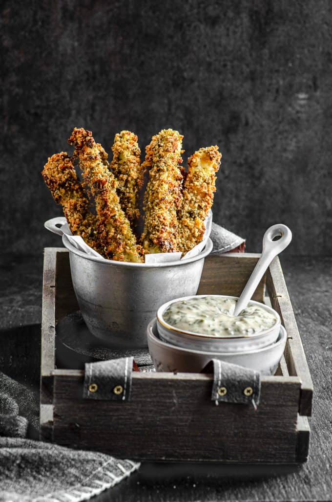 Baked zucchini fries in a fry holder with a small bowl of tahini sauce and a little spoon