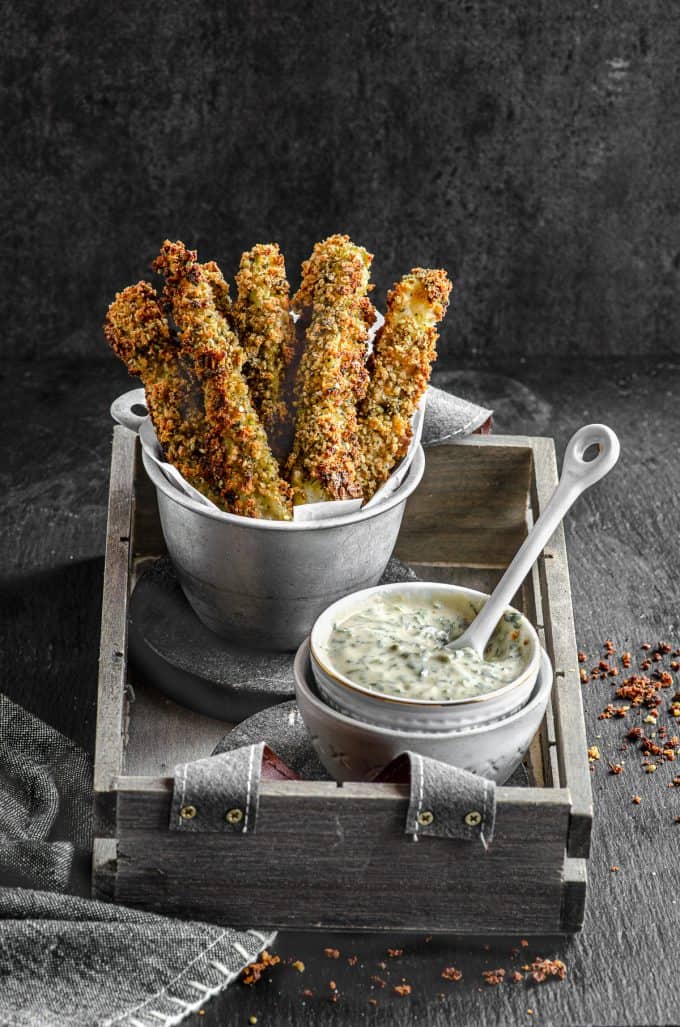 Baked zucchini fries in a fry holder with a small bowl of tahini sauce and a little spoon