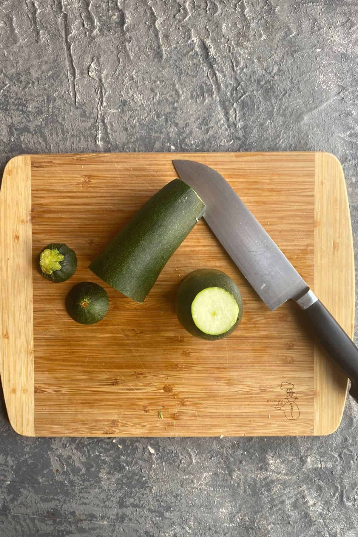 An overhead view of a cutting board with zucchini and three rounds cut off