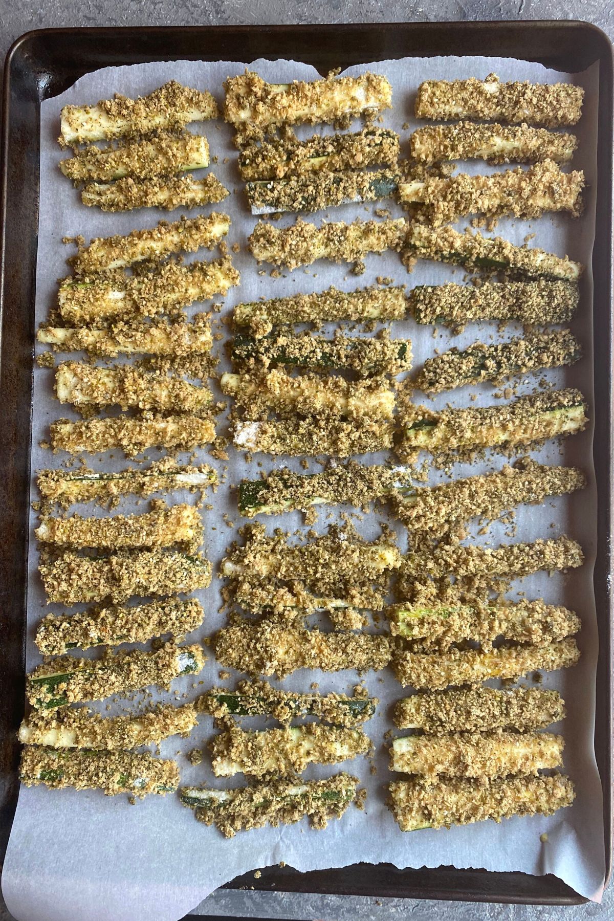 A parchment paper lined baking sheet with zucchini fries lined up ready to bake