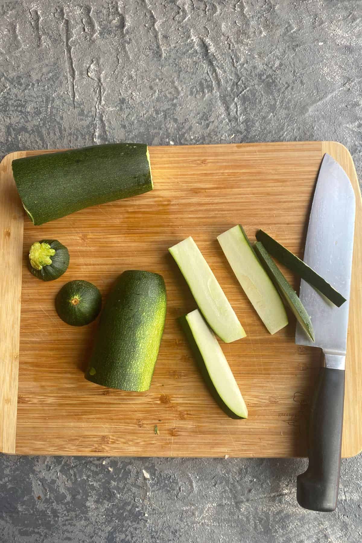 A zucchini on a cutting board cut into three whole pieces with one chopped into fry shape