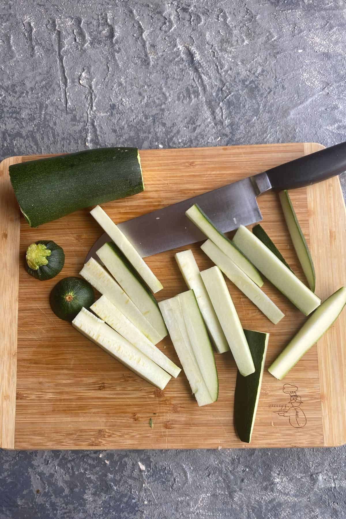 Zucchini being cut into fries on a cutting board