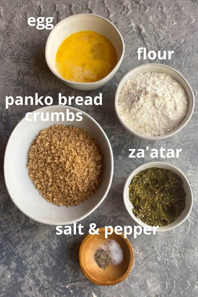 An overhead view of the ingredients to bread zucchini fries; egg, flour, panko bread crumbs, za'atar, salt and pepper