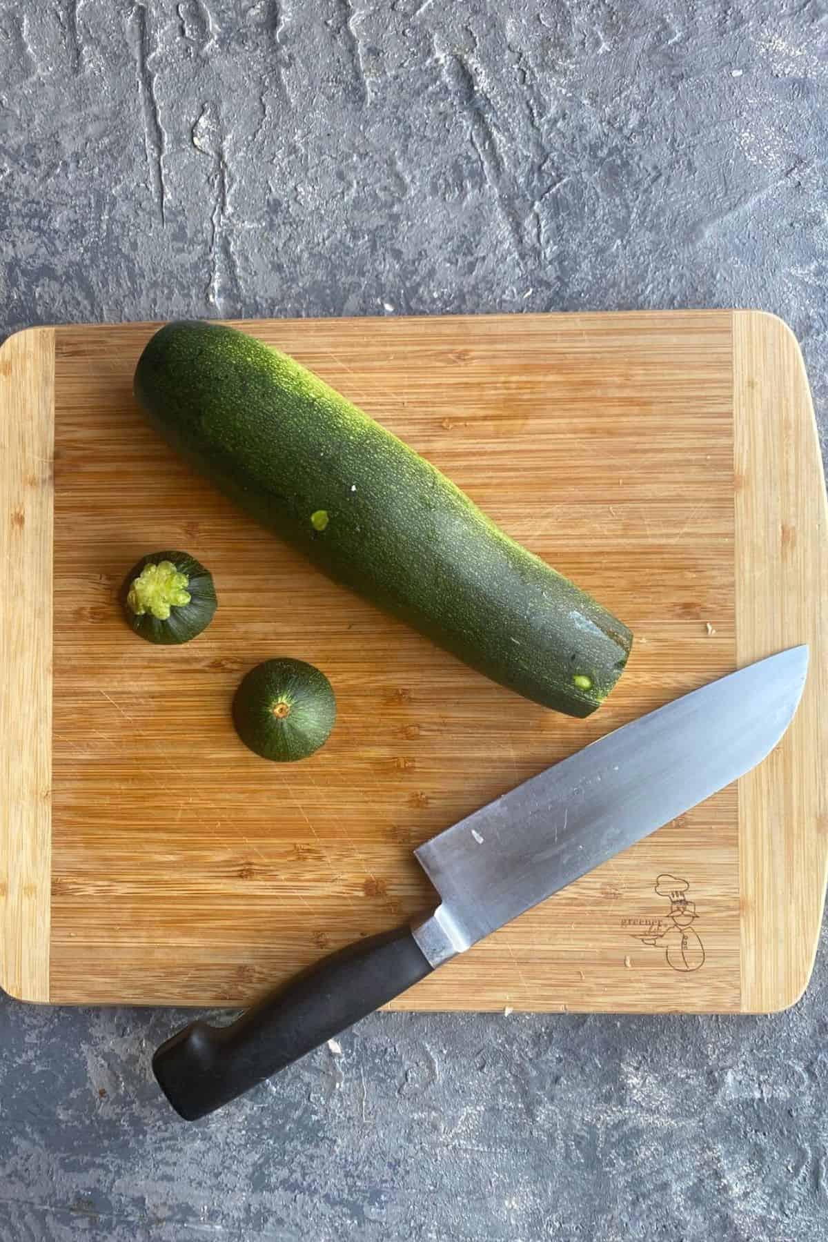 An overhead view of a cutting board with a zucchini with the ends chopped off