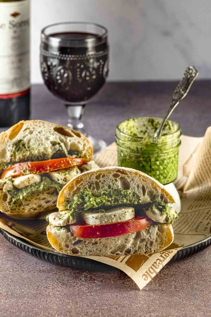 Side view of two caprese sandwich on a plate with a small jar of pesto in the background.