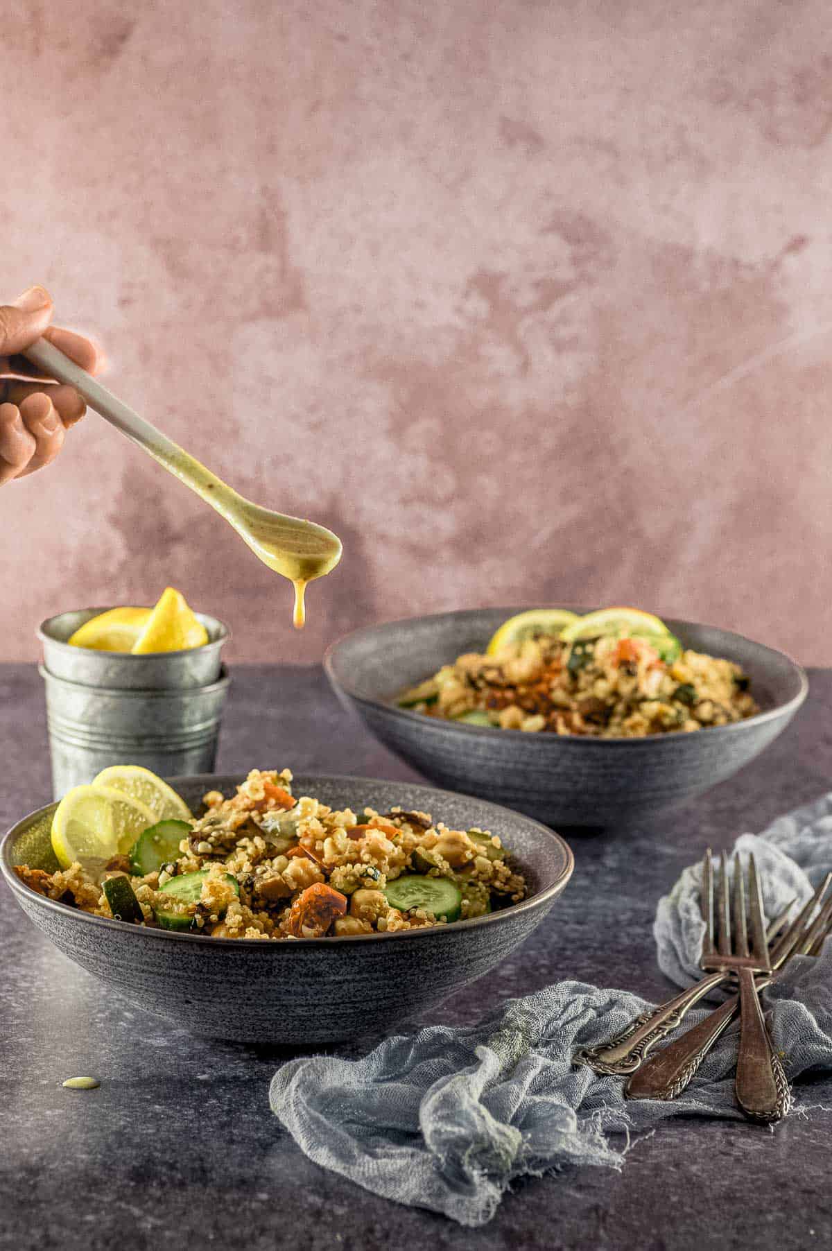 drizzling saad dressing on a bowl of Mediterranean Quinoa salad