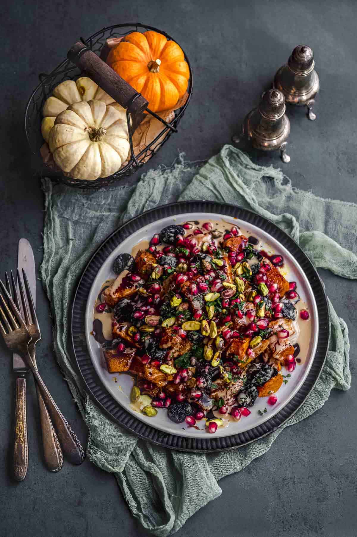 overhead view of a plate with roasted butternut squash with tahini, silan, pomegranates and pistachios