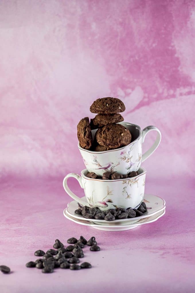 Brownie cookies stacked on top of two tea cups on a pink background