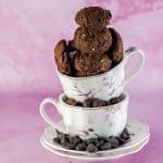 close up of Brownie cookies stacked on top of two tea cups on a pink background