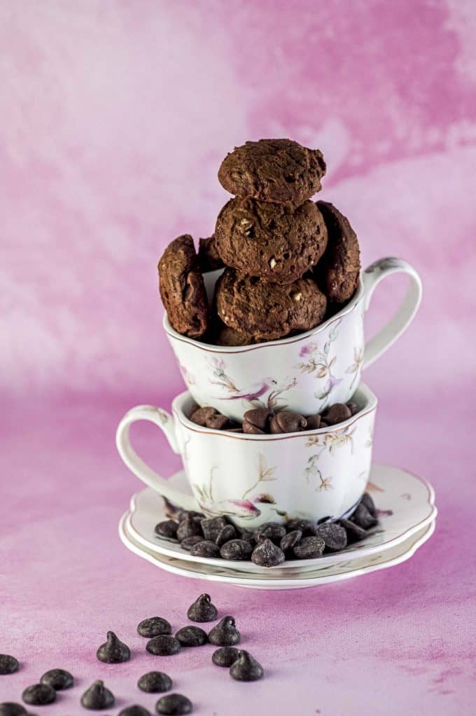 close up of Brownie cookies stacked on top of two tea cups on a pink background