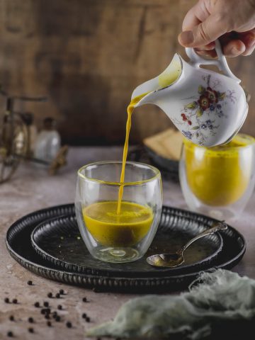 pouring golden milk into a glass cup