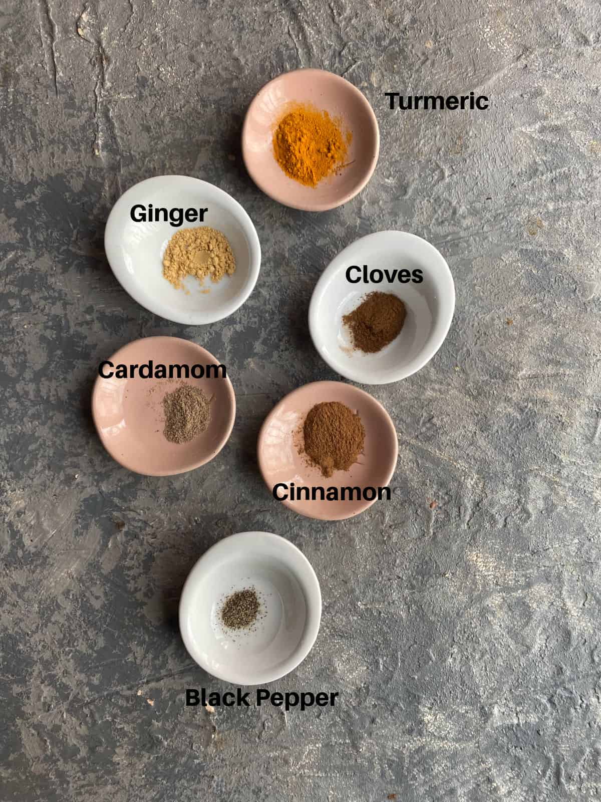 Spices to make golden milk in separate small bowls. Tuemric, cinnamon, ginger, cloves, cardamom and black pepper