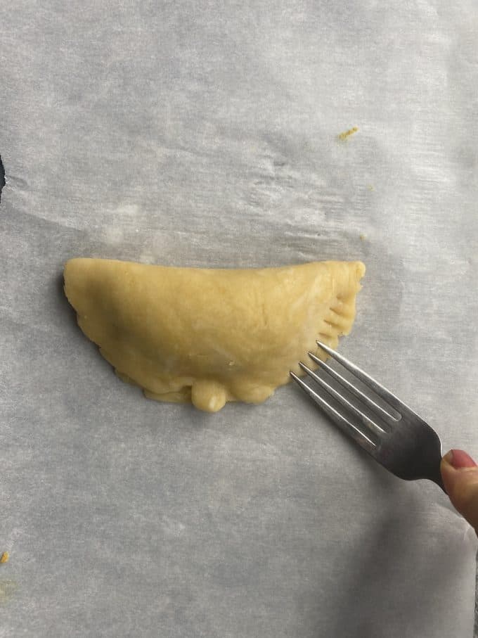 pressing a fork into the edges of the empanada to seal it
