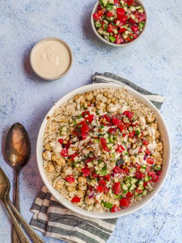 An Israeli salad Quinoa bowl next to a small bowl with tahini dressing
