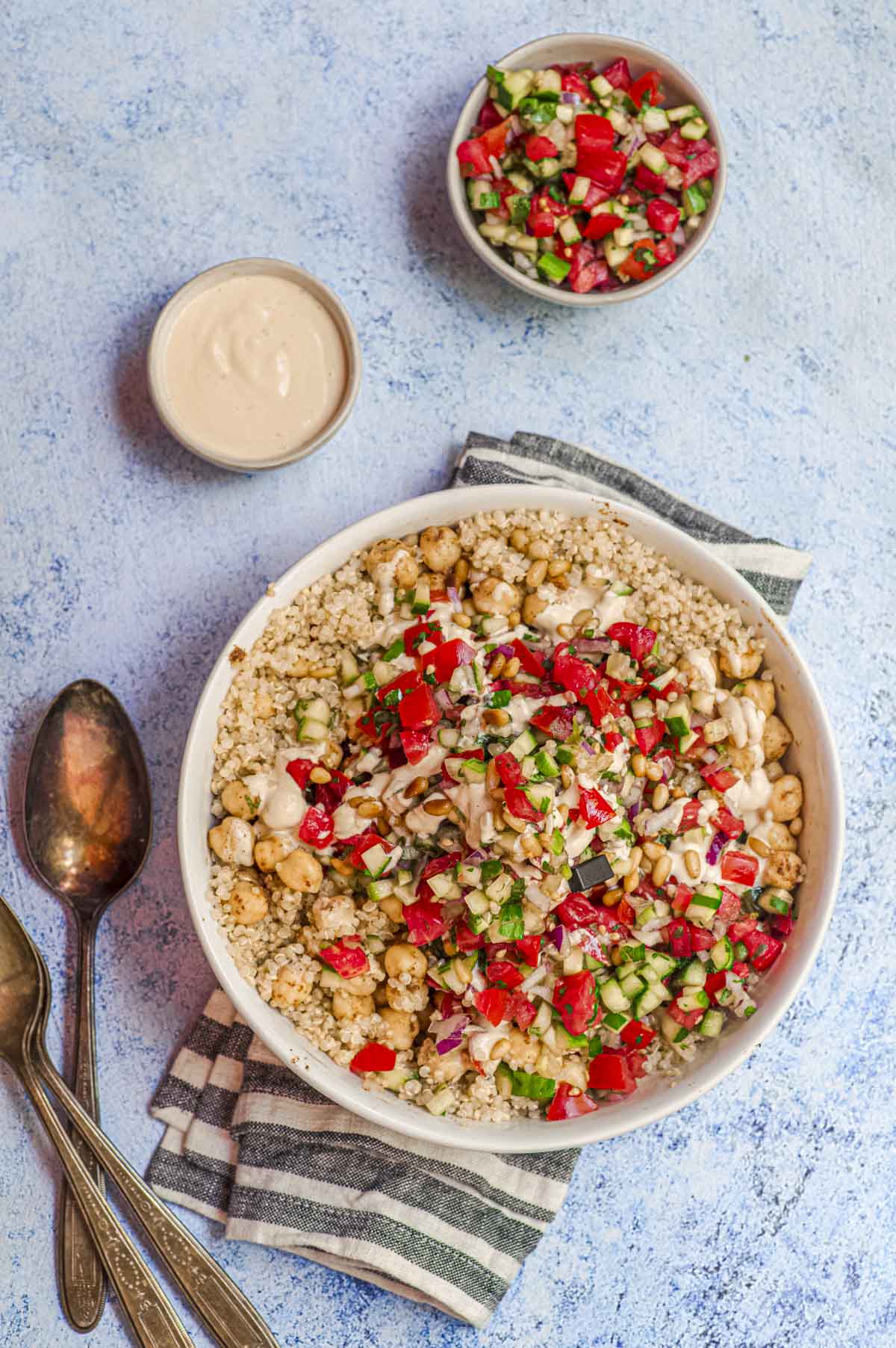 An Israeli salad Quinoa bowl next to a small bowl with tahini dressing